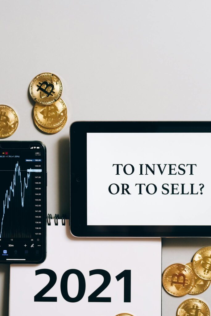 Tablet with 'To Invest or To Sell?' text, gold bitcoins, smartphone displaying a stock chart.